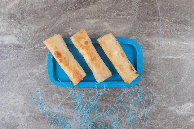 Free photo pancake wrappings on a blue platter on marble surface