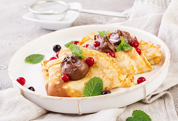 Pancakes with berries and chocolate decorated with mint leaf. Tasty breakfast.