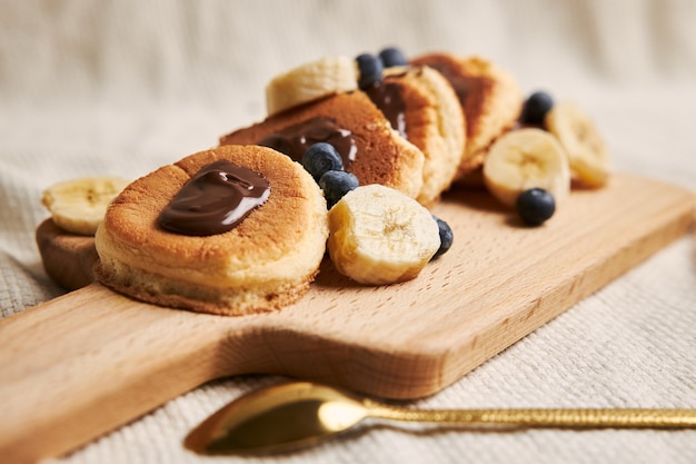 Pancakes with chocolate sauce, berries, and banana on a wooden plate behind a white background