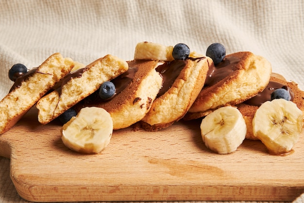 Pancakes with chocolate sauce, berries, and banana on a wooden plate