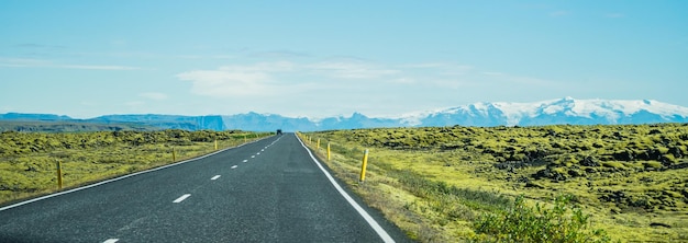 Free photo panoramic of a long asphalt road surrounded by grassy fields in iceland