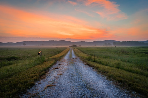 Free photo panoramic shot of a dirt path in the middle of a field with the silhouette of the mountains at dusk