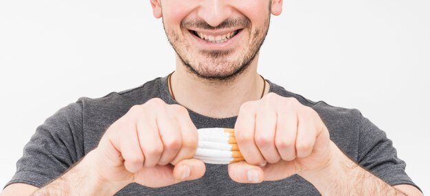 Panoramic view of smiling man breaking cigarettes with two hands