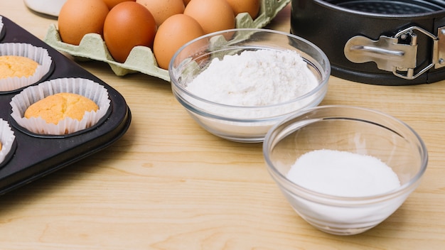 Panoramic view of sugar and flour bowl with eggs and cupcakes on wooden table