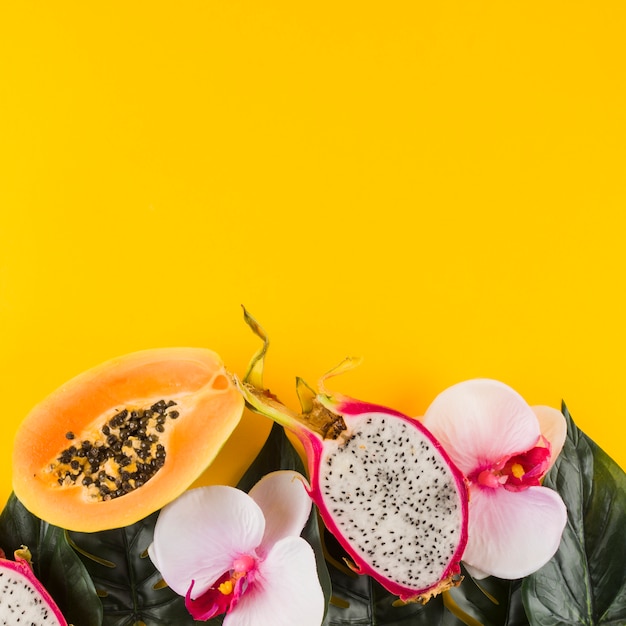 Papaya; dragon fruit; leaves and orchid flower against yellow backdrop