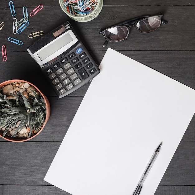 Free photo paper clips; calculator; eyeglasses; potted plant with pen on blank white paper