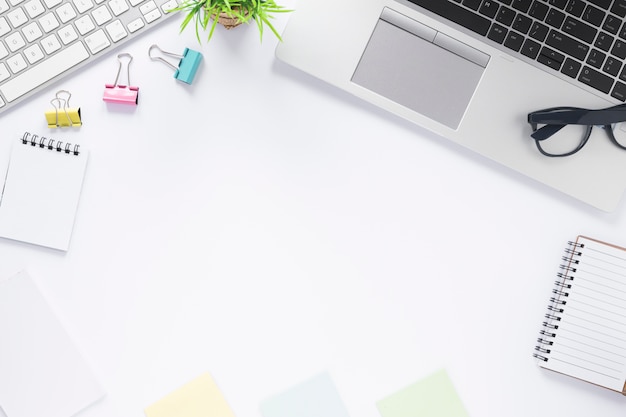 Free photo paper clips; keyboard; laptop; spiral notepad and sticky notes on white desk with space for writing text