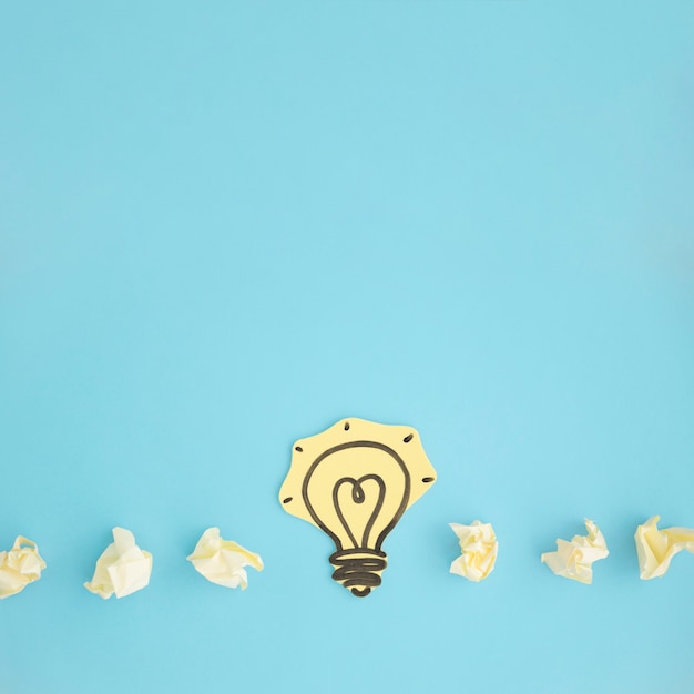 Free photo paper cut out yellow light bulb with crumpled paper on blue background