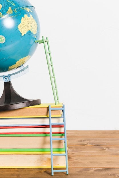 Free photo paper ladder on terrestrial global map stand ball and books on wooden table