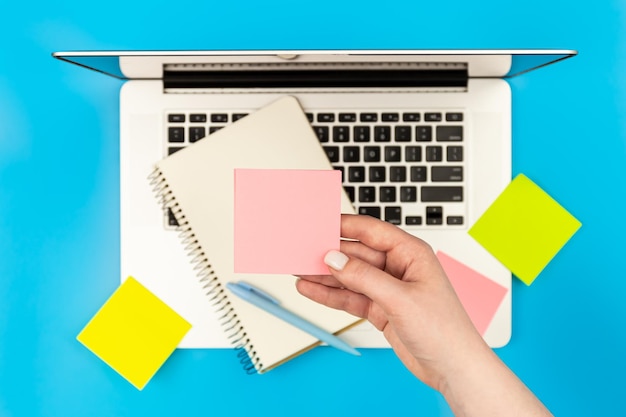 Free photo paper reminder in a female hand against a laptop on a blue background