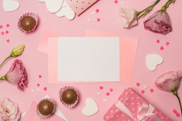 Papers between flowers near present box and chocolate candies