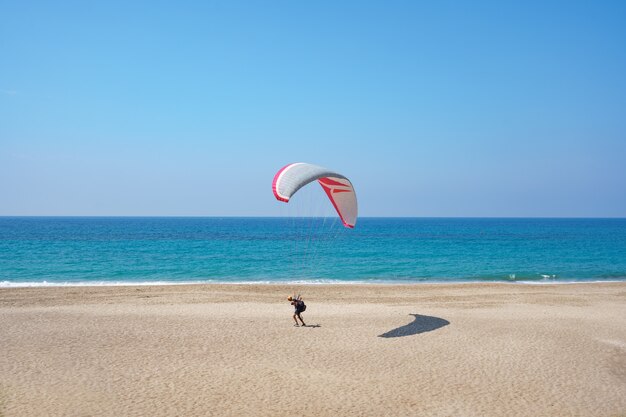 Paraglider flying over the sea shore with blue water and sky on horison. View of paraglider and Blue Lagoon in Turkey.