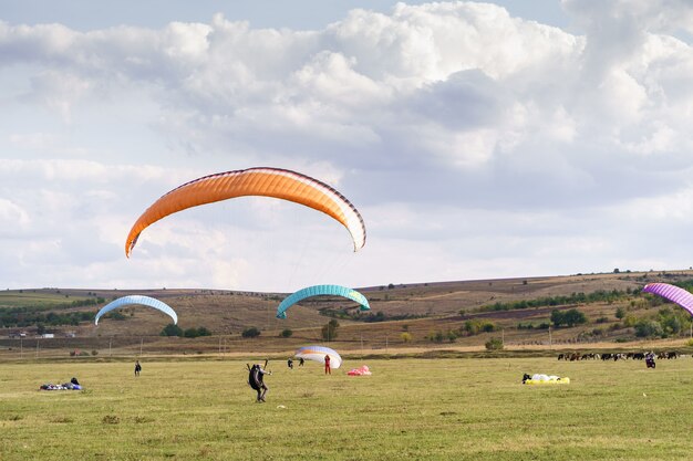 Paragliders silhouette flying over beautiful green landscape under blue sky with clouds.