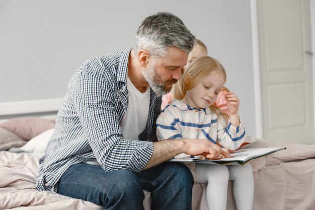 Parenthood. Cute girl sitting with grandpa in the bedroom. Reading together a book.