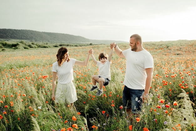 Parents are holding their son for hands among the poppies field