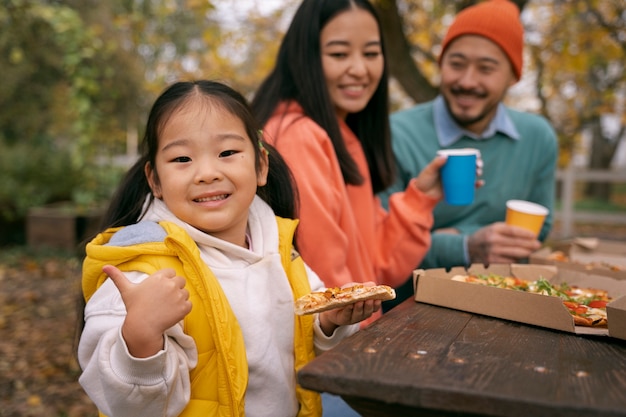 Free photo parents and kid eating pizza outdoors side view