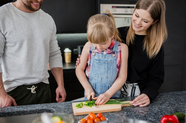 Free photo parents looking at girl cutting vegetables