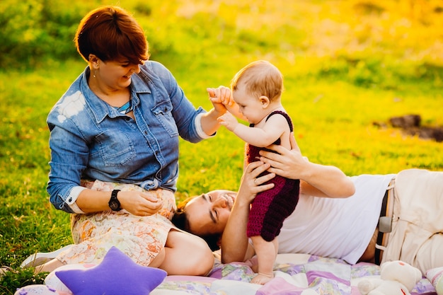 Free photo parents and their little daughter lie on the blanket on green lawn