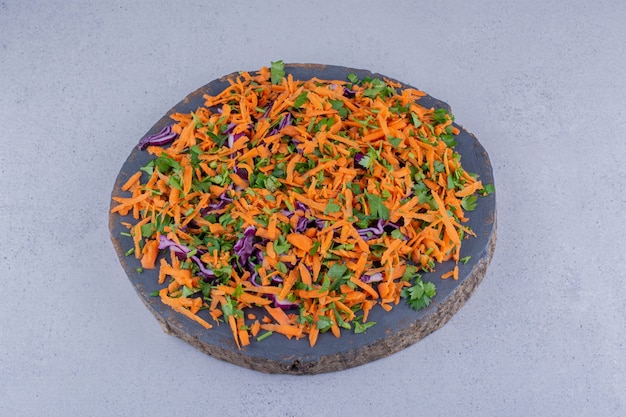 Parsley, carrot and red cabbage chopped into a salad on a board on marble background.