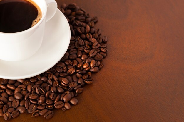 Partial view of coffee cup and beans on wooden table