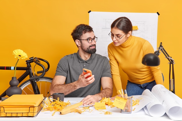 Partnership and communication concept. Skilled woman and man office workers work on designing graphic pose at messy desktop with blueprints generate creative ideas for future architectural project