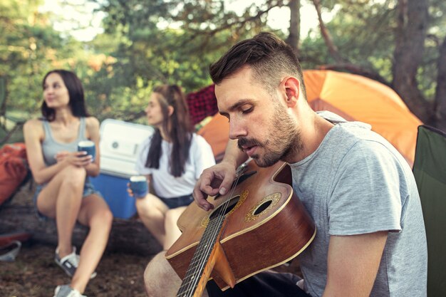 Free photo party, camping of men and women group at forest. relaxing, singing a song against green grass.