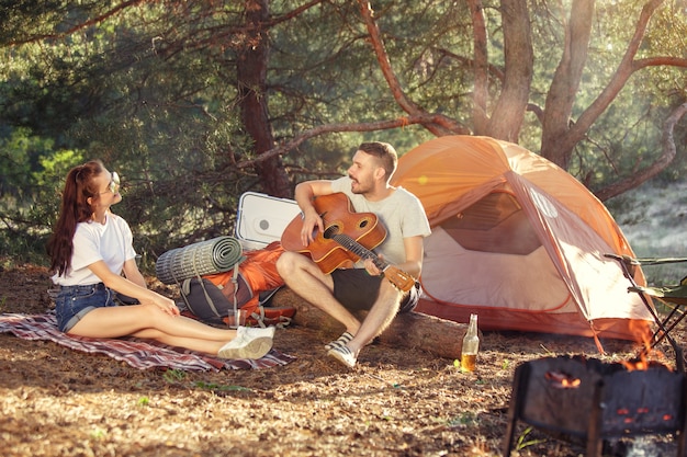 Party, camping of men and women group at forest. They relaxing, singing a song against green grass. concept