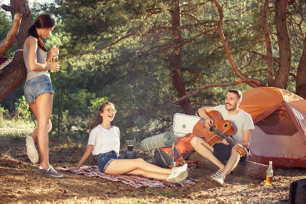 Party, camping of men and women group at forest. They relaxing, singing a song against green grass. The vacation, summer, adventure, lifestyle, picnic concept