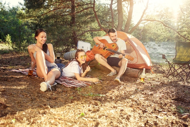 Free photo party, camping of men and women group at forest. they relaxing, singing a song against green grass. the vacation, summer, adventure, lifestyle, picnic concept