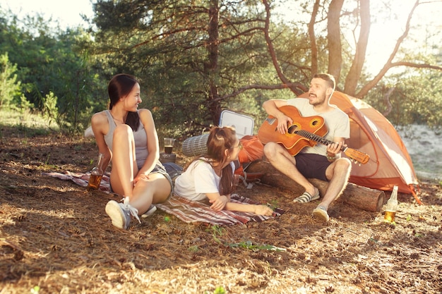 Party, camping of men and women group at forest. They relaxing, singing a song against green grass. The vacation, summer, adventure, lifestyle, picnic concept