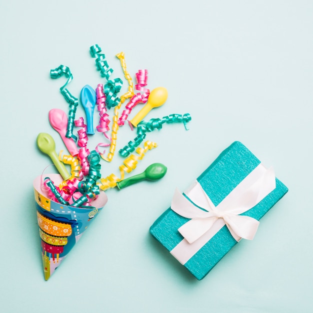 Free photo party hat with streamers; balloons and wrapped present on blue backdrop