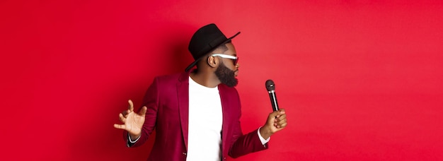 Free Photo passionate black male singer performing against red background singing into microphone wearing party