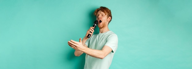 Free Photo passionate redhead man in tshirt singing serenade with microphone looking aside at karaoke and gestu