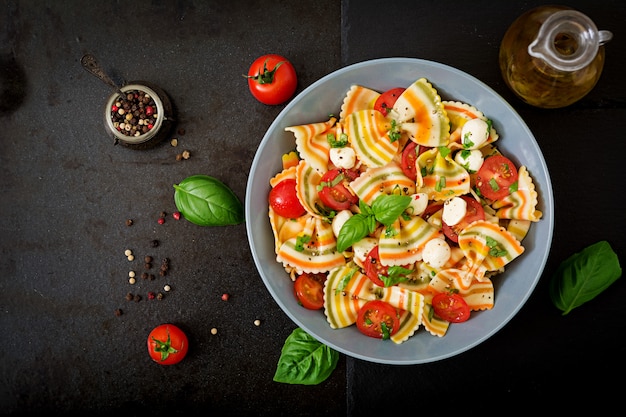 Pasta colored farfalle salad with tomatoes, mozzarella and basil.