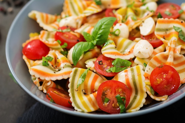 Free photo pasta colored farfalle salad with tomatoes, mozzarella and basil.