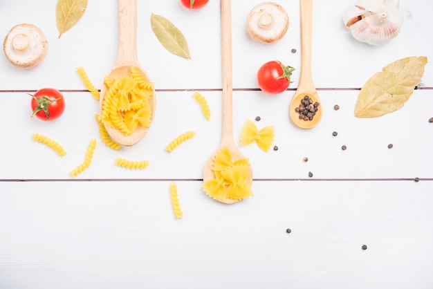 Free photo pasta ingredients with spices and vegetables on white plank table