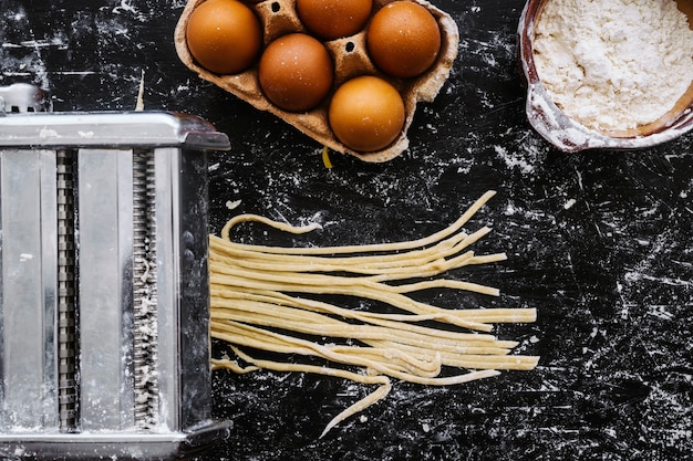 Free photo pasta machine cutting dough near ingredients