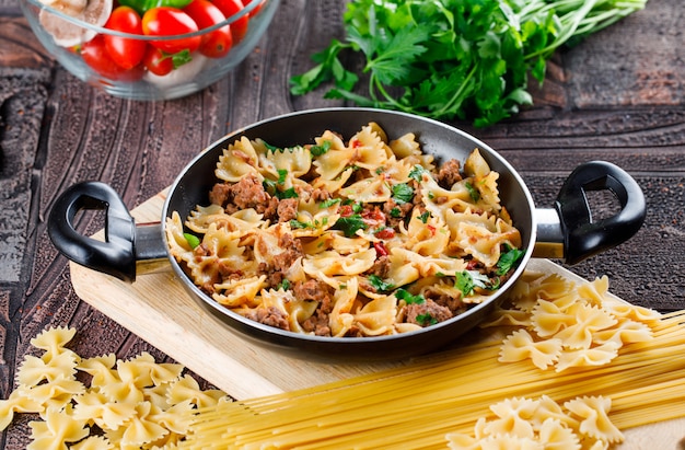 Free photo pasta meal in pan with raw pasta, mushroom, parsley, tomato