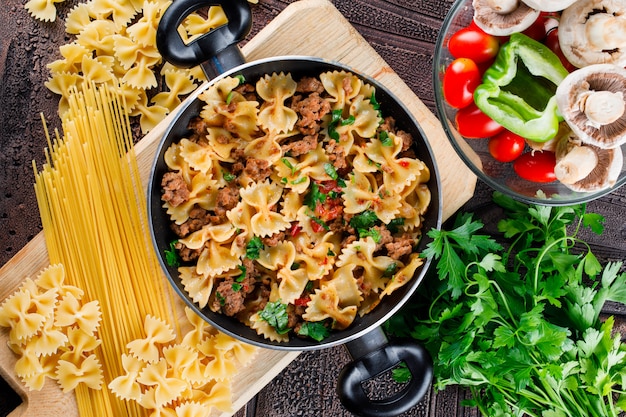 Free photo pasta meal in pan with raw pasta, mushroom, pepper, parsley, tomato