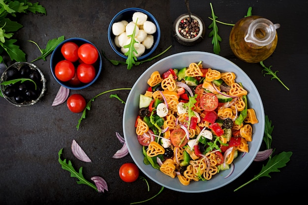 Free photo pasta in the shape heart salad with tomatoes, cucumbers, olives, mozzarella and red onion greek style. flat lay. top view