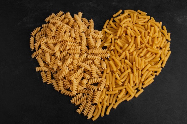 Pasta varieties in heart shape on black surface. 