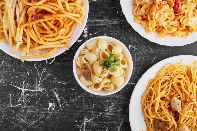 Pasta varieties in tomato sauce in a white plate on black background. 