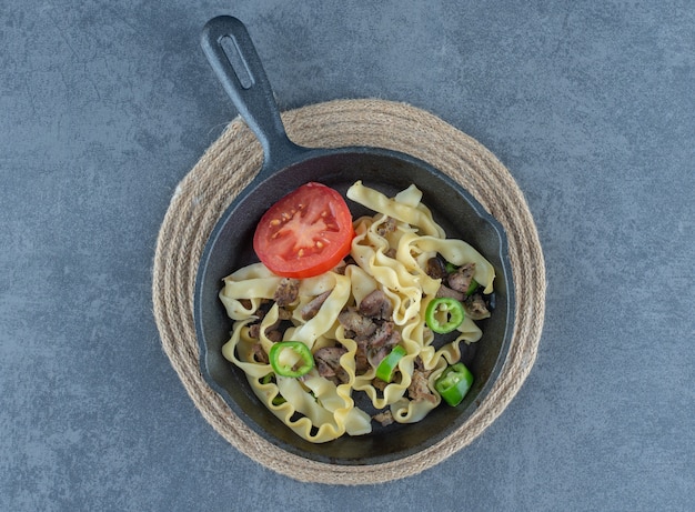 Free photo pasta with beef parts on black pan.