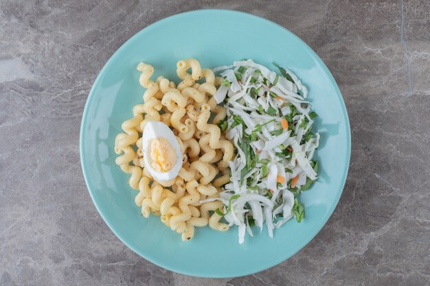 Pasta with fresh salad and egg on blue plate.