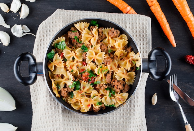 Free photo pasta with meat in a pan with onion, garlic, carrots, fork, knife