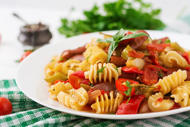 Free photo pasta with tomato sauce with sausage, tomatoes, green basil decorated in white plate on a wooden table.