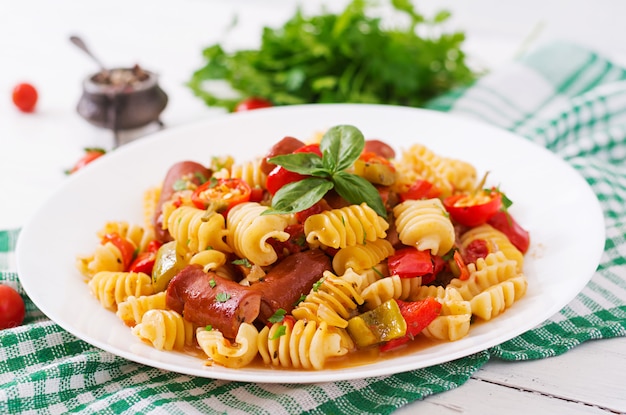 Pasta with tomato sauce with sausage, tomatoes, green basil decorated in white plate on a wooden table.