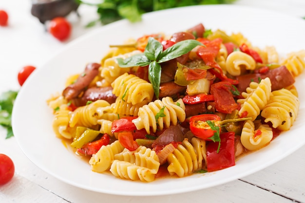 Pasta with tomato sauce with sausage, tomatoes, green basil decorated in white plate on a wooden table.