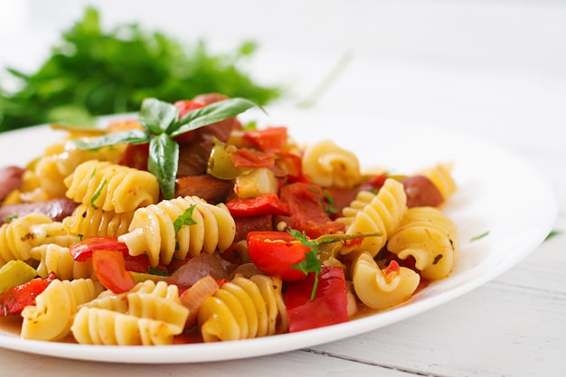 Pasta with tomato sauce with sausage, tomatoes, green basil decorated in white plate on a wooden table.