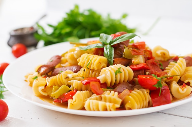 Free photo pasta with tomato sauce with sausage, tomatoes, green basil decorated in white plate on a wooden table.